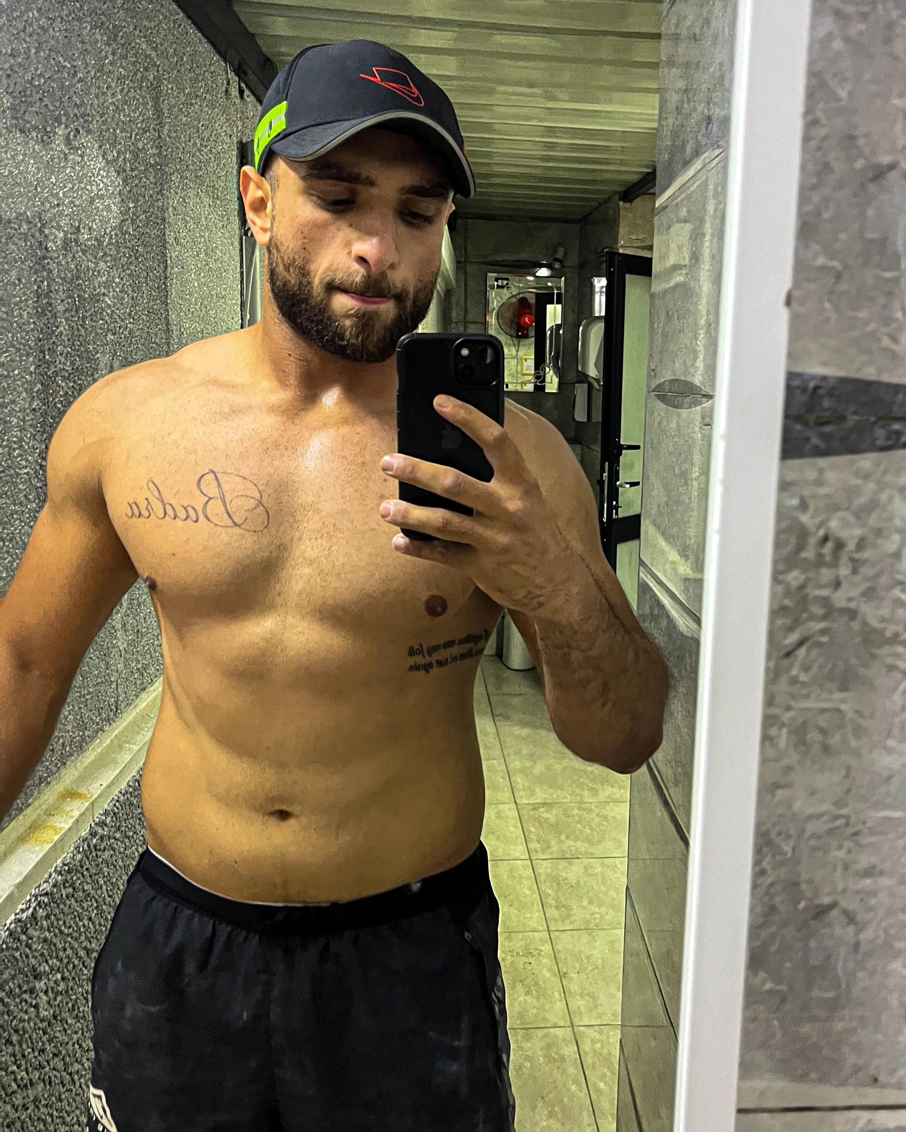 Ramez Asaad, shirtless in a cap, taking a mirror selfie in the gym