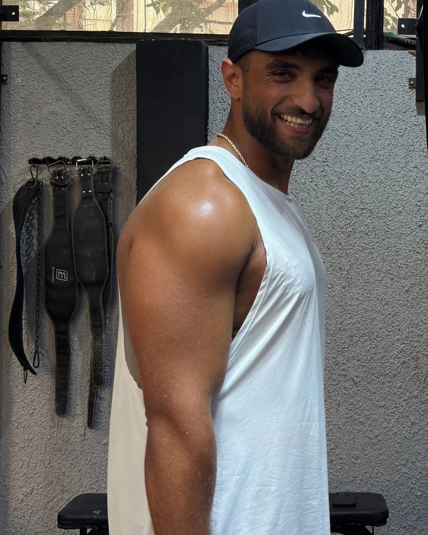 Ramez Asaad smiling in a white training tank and cap in the gym